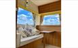 Inside area of the vintage caravan. Seating area with a small wooden table and 2 large windows with floral curtains