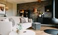 Stylish modern living room with a neutral-toned sofa, patterned cushions, hanging fireplace, and warm accent lighting against a dark textured feature