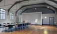 Large room with polished wood floors, beams and seating around a large table.