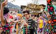 Members of 'Loud Noises' dancing, playing the trumpet, wearing vibrant patterned costumes and giving a lively performance to a crowd