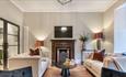 Light coloured living area with a fireplace as a focal point. 2 Large beige sofas place either side of a black coffee table and 2 navy armchairs