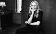Black and white photo of Lucy Foley smiling, resting her head in her right hand. Credit Jesse Dittmar
