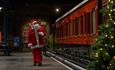 Satna Claus walking along the platform at Locomotion which is decorated with a Christmas tree.