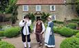 Image of three people dressed in antiquated attire outside Pockerley Old Hall at Beamish Museum