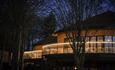 Exterior view of Treehouses at night, nestled in woodland and decorated with warm white lighting.