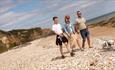 Three people walking on beach with dog