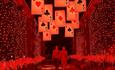 Adventures in Wonderland. Two people walking through a red tunnel of lights, beneath suspended playing cards.