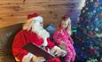 Santa reading to a little girl by a Christmas Tree.