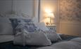 Vintage style white bedframe with bathrobes place on top. White panelled walls and blue patterned wallpaper.