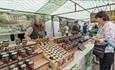 Chutney trader at Barnard Castle Farmers' market. Woman looking at chutneys and holding her purse.