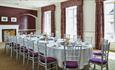 Bowes room set up boardroom style
Long table with white chairs and purple seat pads. 
Dark red chimney breast, light walls with red, patterned curtain