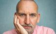 Christopher Eccleston headshot, resting his head in his right hand.