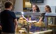 two women smiling at customers from behind serving fridge at Durham Cathedral Undercroft Restaurant.