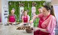 Four people participating in a chocolate making workshop.  One person is mixing a bowl of dark chocolate and the other three are watching.