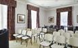 Neville room set up theatre style with white chairs
Light coloured walls with dark red, patterned curtains on 3 windows