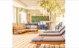 Spa area with wooden floor. Wooden loungers with grey padded seating.
A large decorative tree in the background.