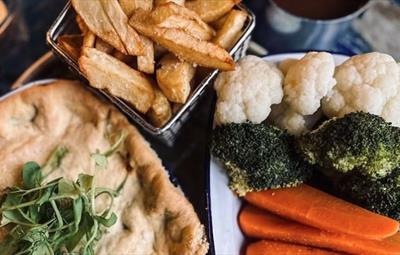 Close up of pie with salad garnish on top, next to chips and plate of vegetables