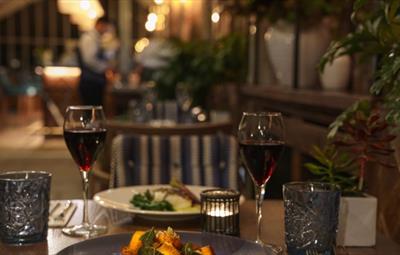 Two meals, candle and two filled wine glasses on restaurant table.