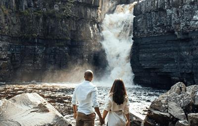 Couple holding hands, admiring High Force Waterfall.