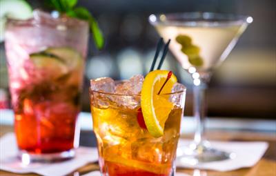 Three different types of colourful cocktails, one with a lemon garnish, another with a a mint garnish.