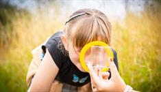 Girl looking through a magnifying glass into a bug pot