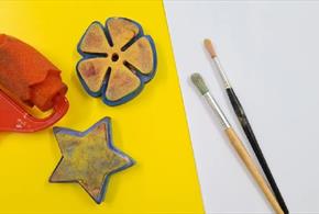 Two paint brushes, a flower and star shape for printing with paint and a print roller