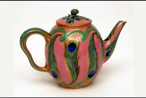 A colourful teapot with peacock feathers painted onto it.