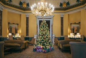 Christmas tree with presents under an opulent candelabra in a comfortable lounge area.