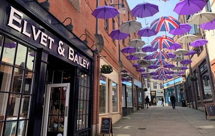 Union Jack and purple and white umbrellas suspended above Prince Bishops Place with the Elvet & Bailey shop in the foreground.