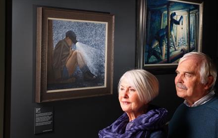 Image of a couple visiting the Mining Art Gallery, Bishop Auckland, and looking at paintings of coal miners.