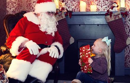 Santa giving a present to a little girl in his grotto at The Bowes Museum.