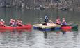 2 red canoes and 1 green canoe filled with children around a floating pontoon