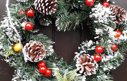 Image of a festive wreath with traditional red berries and pine cones.