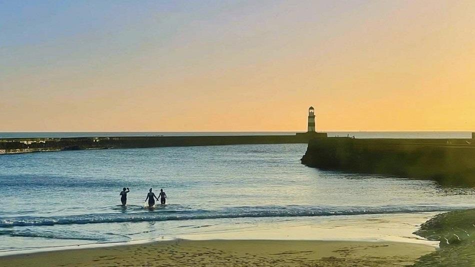 Silhouette of three people swimming at dawn - Seaham Slope Beach, near the pier.
