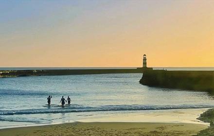 Silhouette of three people swimming at dawn - Seaham Slope Beach, near the pier.