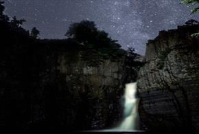Image of a starry sky illuminating High Force Waterfall at night.