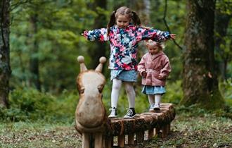 Two children playing on wooden sculpture.