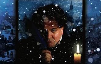 Dark image of actor playing Scrooge with lit candle.