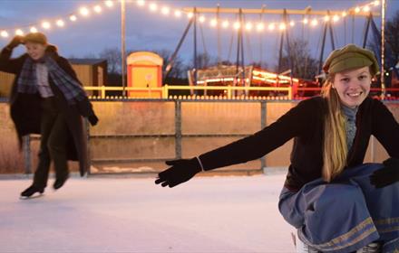 Image of two people skating on the ice rink at Beamish on an evening, surrounded by fairy lights.