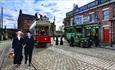 Beamish Museum 1900s Town. 2 People in Victorian Clothes Standing in the Cobbled Streets In front of a Tram.