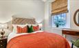 A double bed with orange bedspread. dark wood furniture and circular mirror on the wall