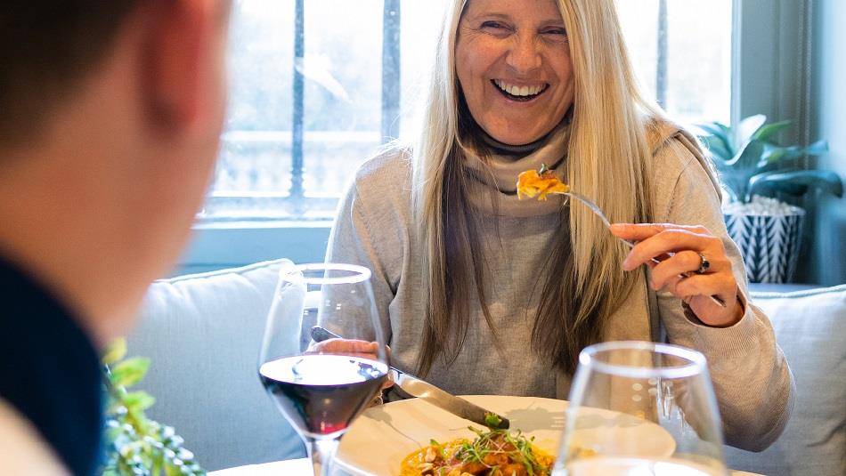 A woman enjoying food and wine in a light, airy dining space.