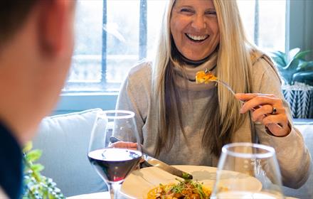 A woman enjoying food and wine in a light, airy dining space.