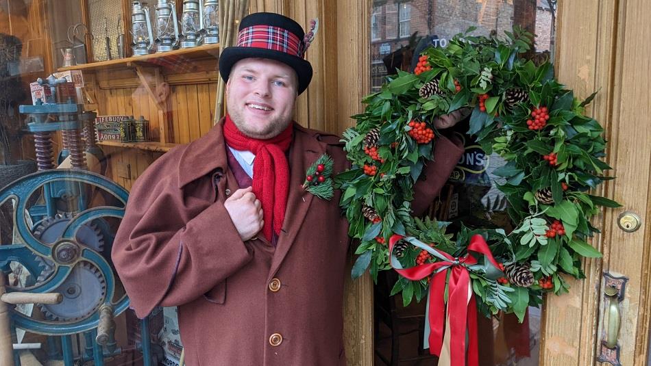 Man dressed in Victorian Clothing holding a Christmas wreath