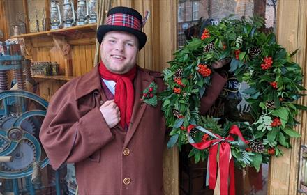 Man dressed in Victorian Clothing holding a Christmas wreath