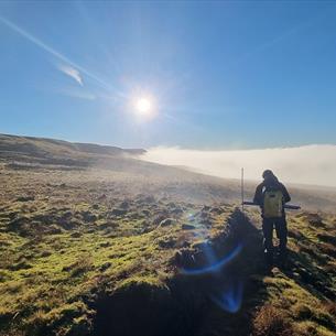 A person walking the North Pennines National Landscape on a sunny day, looking out at the clouds. 