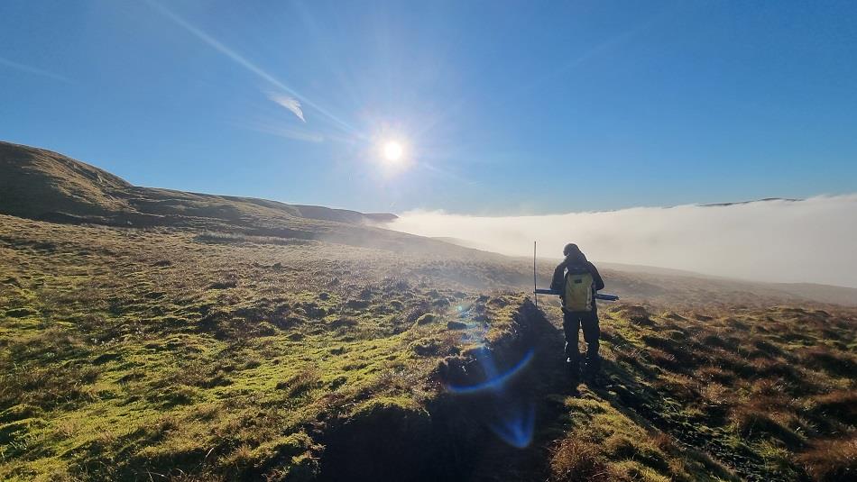 A person walking the North Pennines National Landscape on a sunny day, looking out at the clouds.