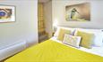 Double bedroom with light coloured walls. Bright yellow bed spread and pictures of a bird and an abstract pattern on the wall.
