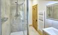 Bathroom with light coloured walls. Wooden door and unit. Walk in shower and spotlights in the ceiling.