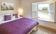 A double bedroom with purple bedspread. Light coloured walls with wooden shutters at the window. A flowery canvas on the wall.
